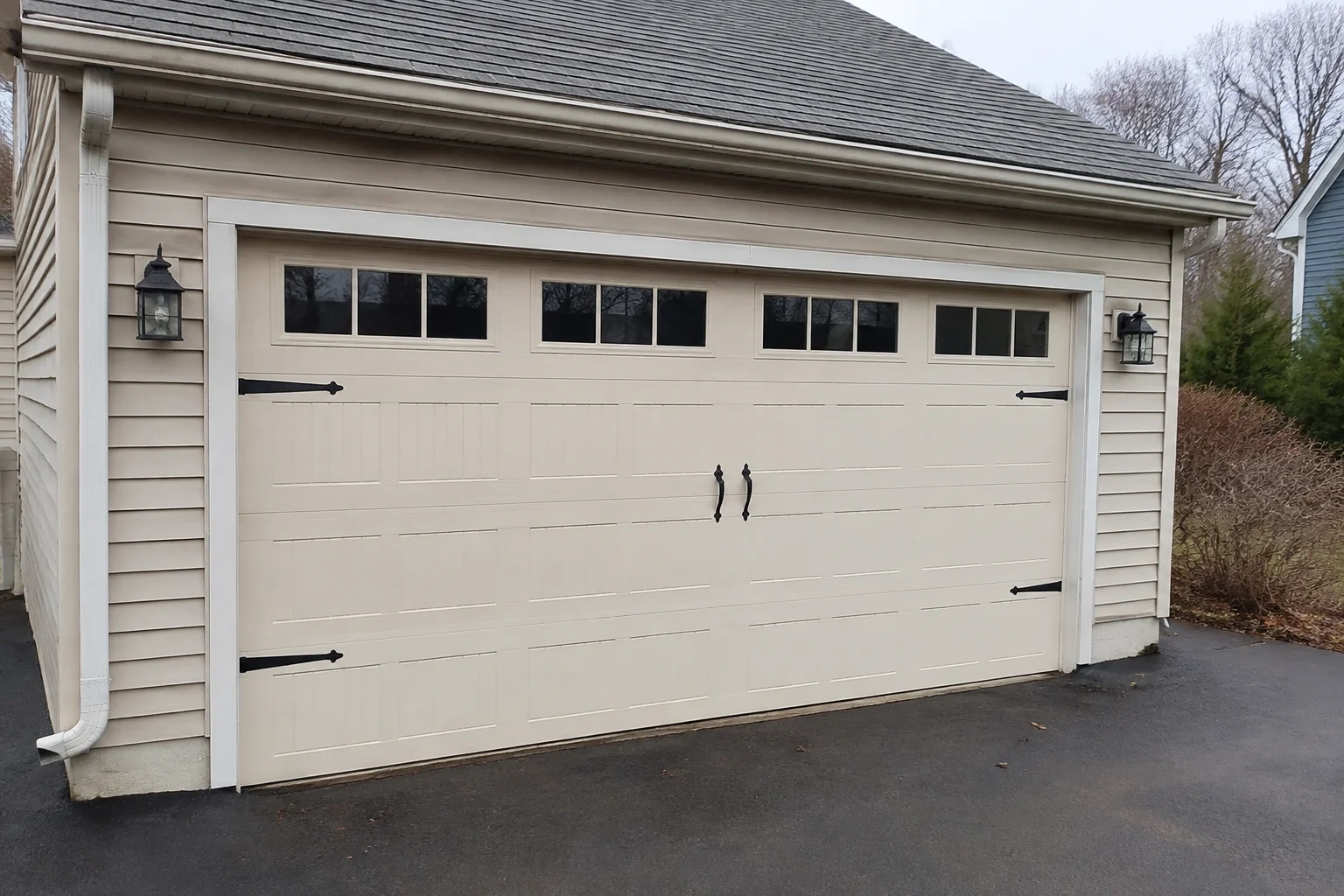 Cream carriage-house-style garage door with dark decorative hardware.
