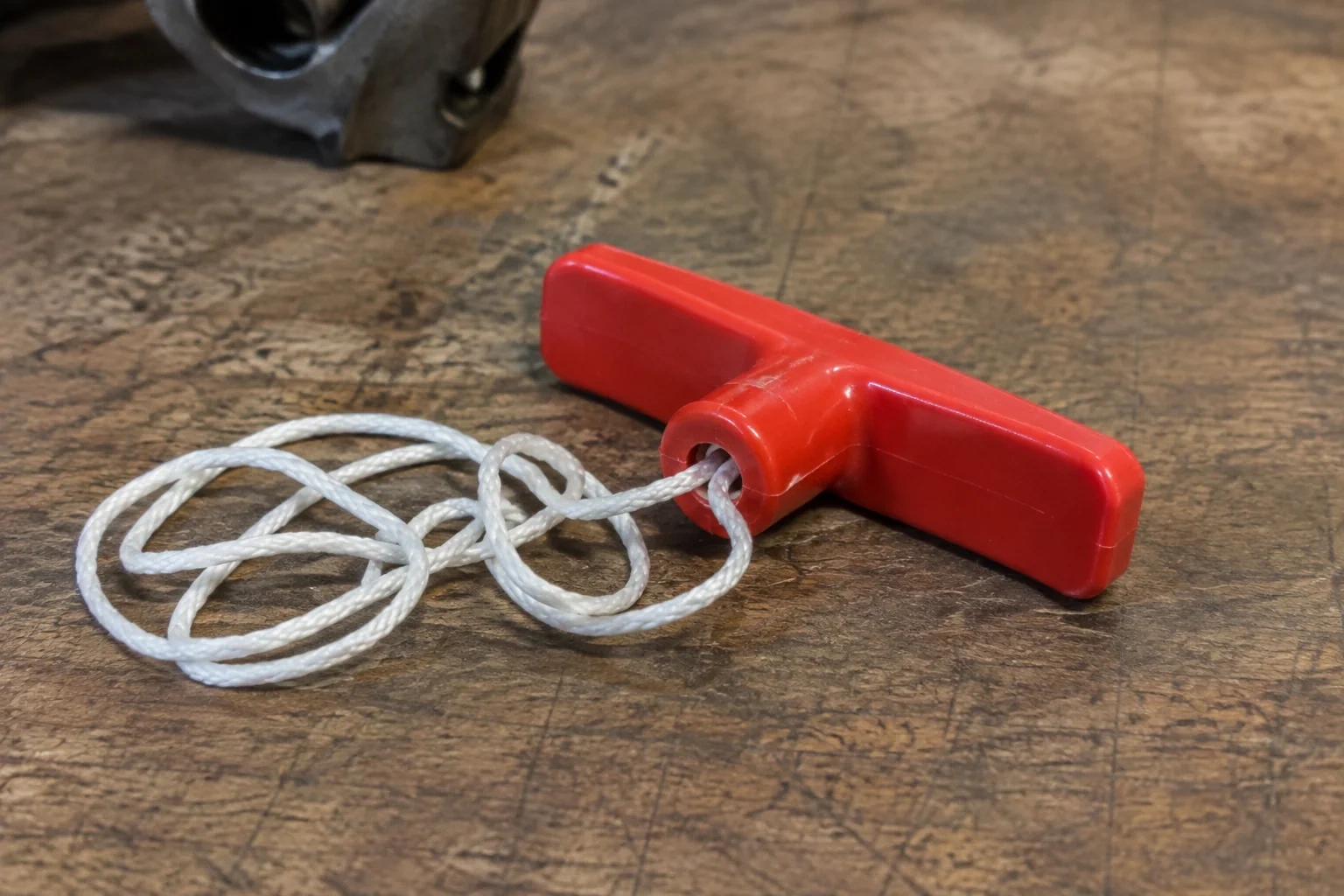 Detached red T-shaped handle with loose white cord on a wooden bench.