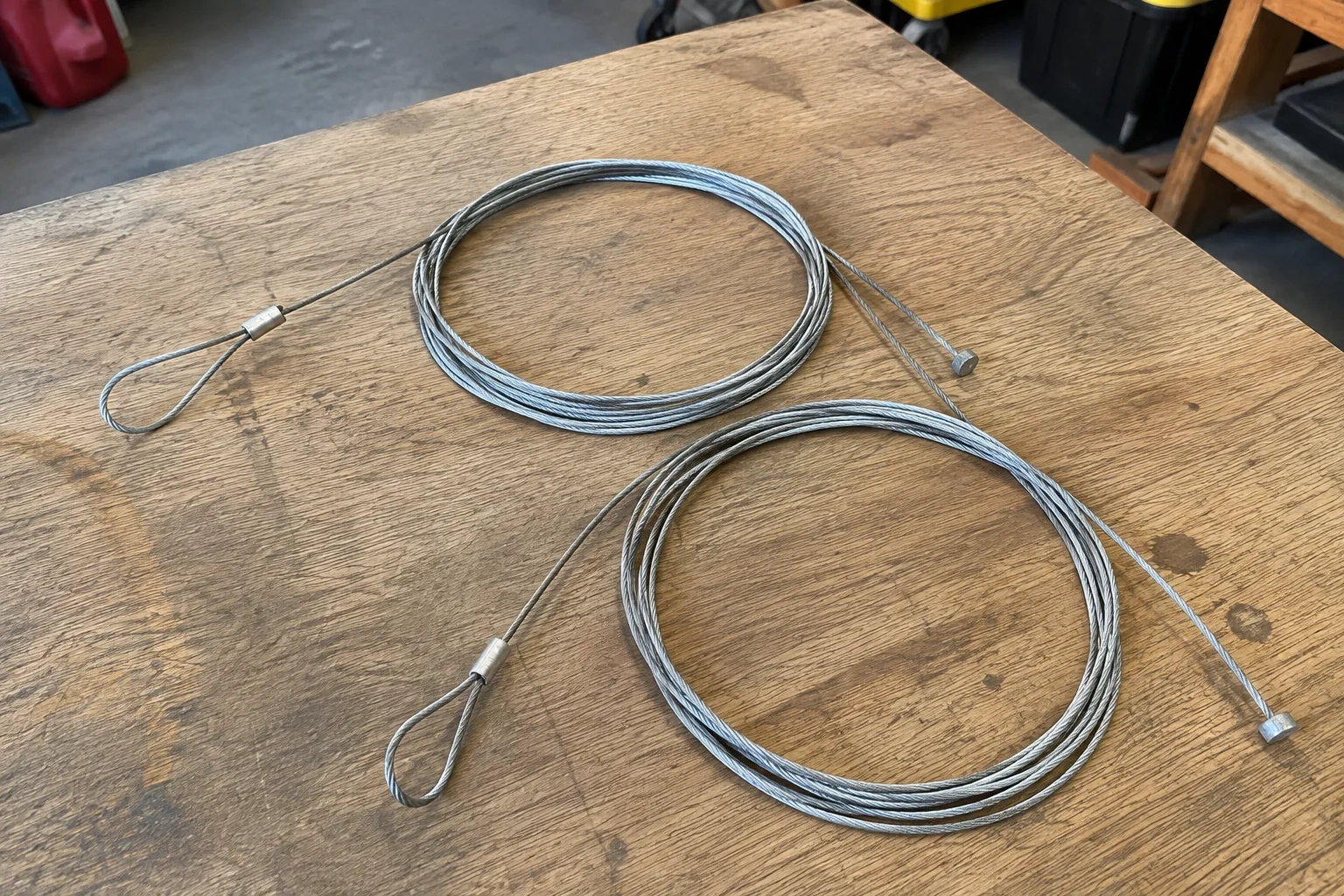 Two coiled steel cables with loop and stop ends on a workbench.