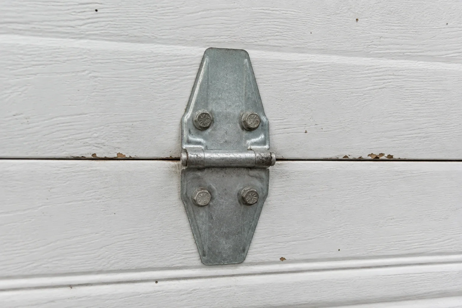 Metal center hinge across a seam in a white sectional garage door.