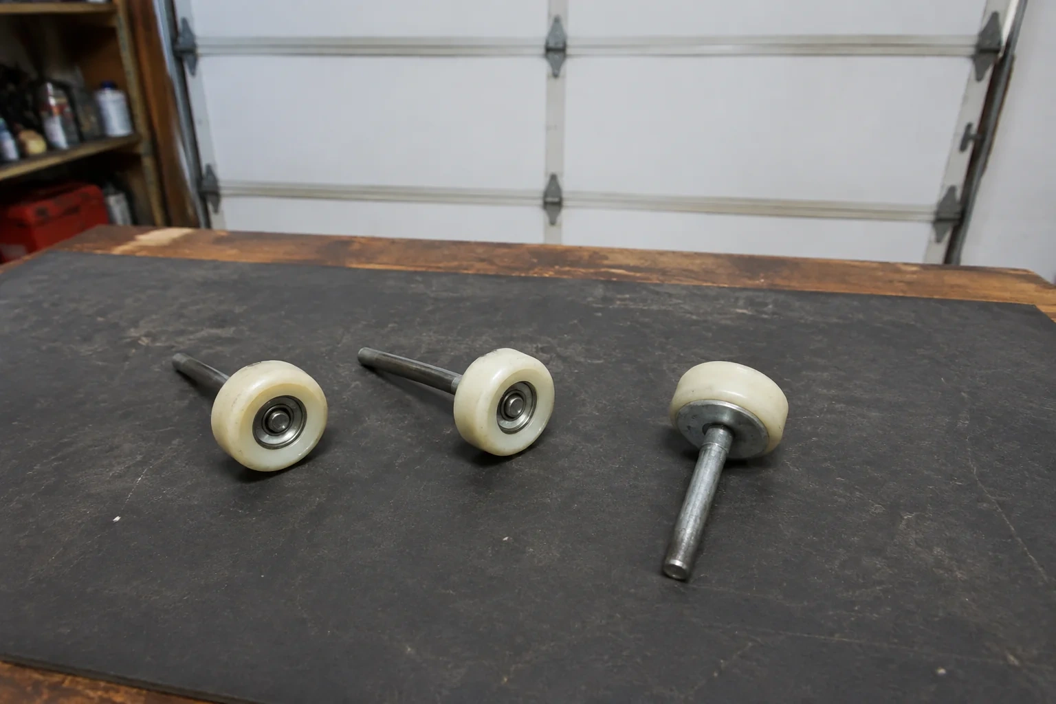 Three detached nylon-wheel garage door rollers with steel stems on a work mat.